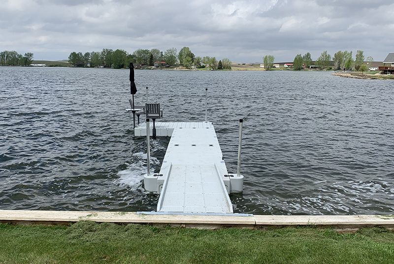 Dock extending into a lake on an overcast day, with houses and trees in the distance.