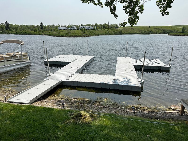 A white floating dock on a lake, accessible from a grassy shore. A boat is docked nearby.