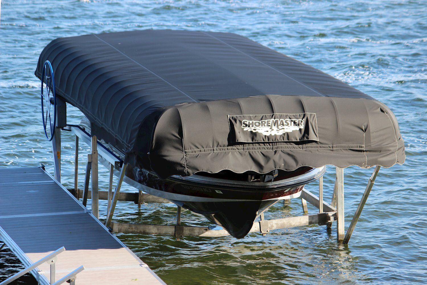 Boat in black cover on a lift at a dock, water in the background.