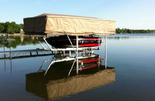 Boat lift with a red and black boat on a lake, with a tan canopy.