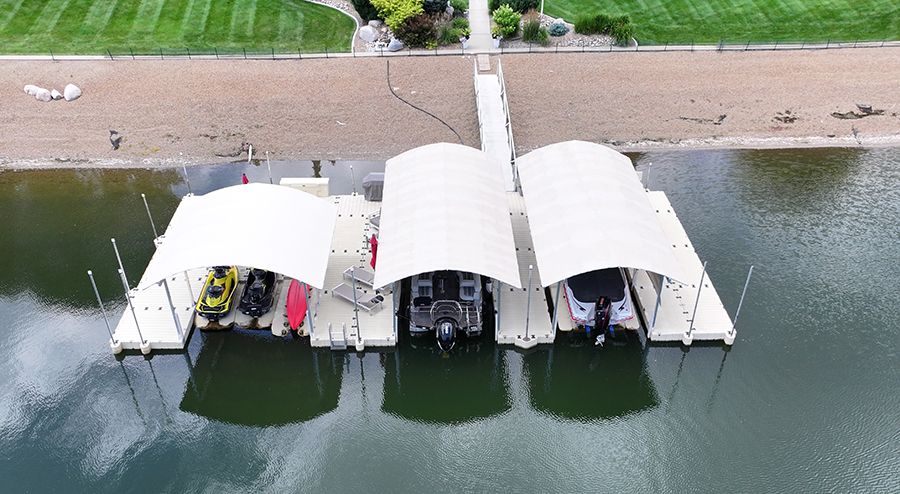 Overhead view of three covered boat docks on a body of water, with boats and a jet ski docked.