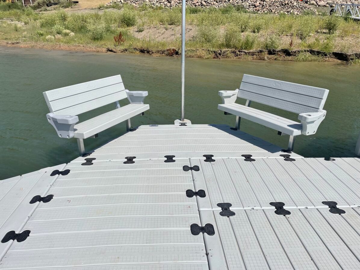 two white benches on a dock next to a body of water