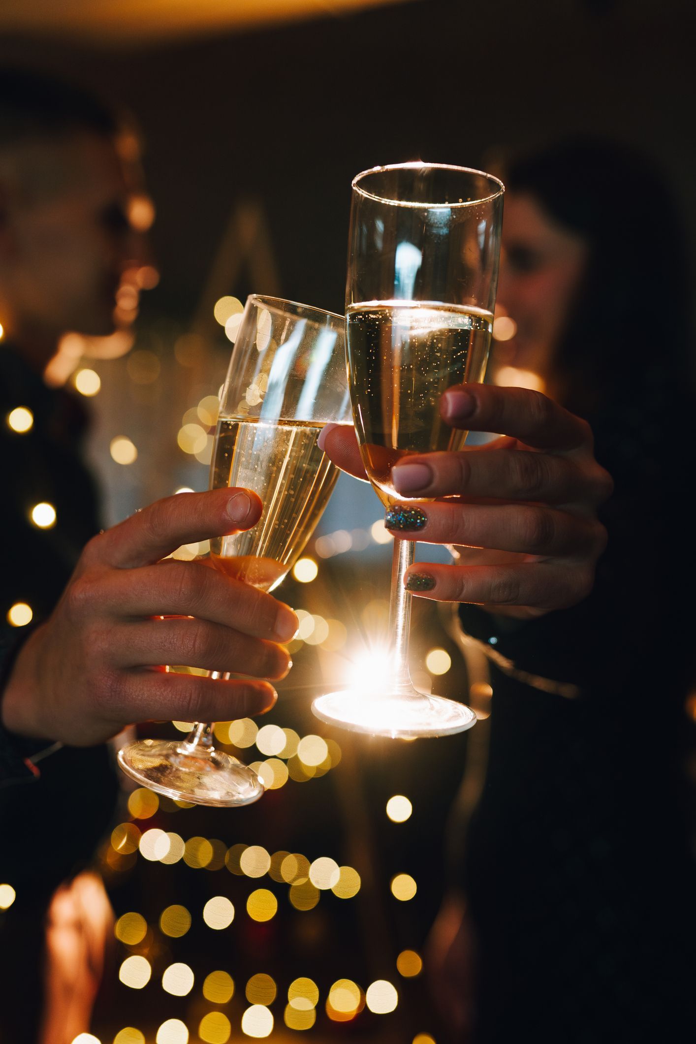 Persone che brindano con calici da champagne; lucine sullo sfondo.
