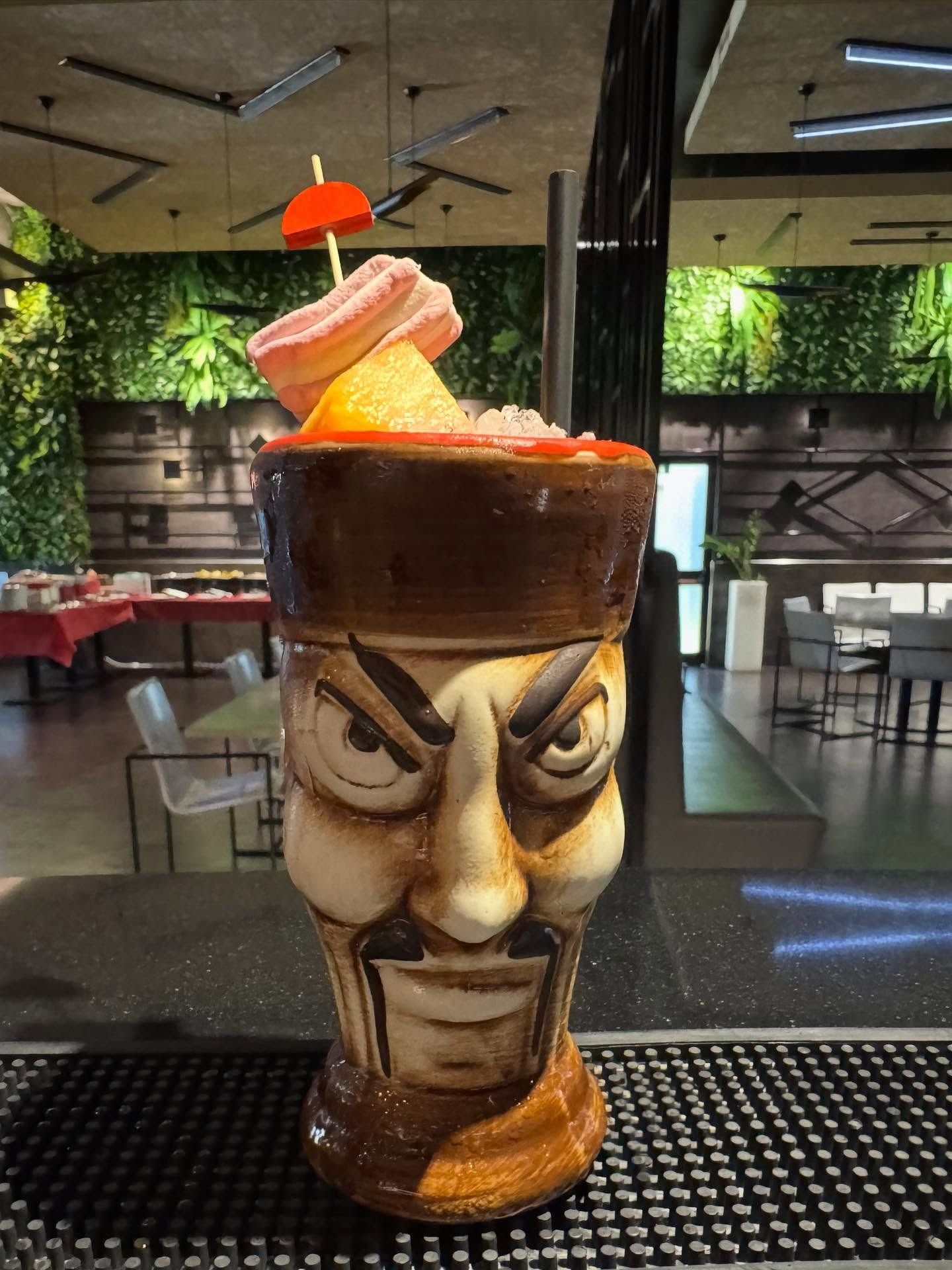 Un panino affettato ripieno di carne, formaggio e condimenti, su un tagliere nero, con una bottiglia di birra sullo sfondo.