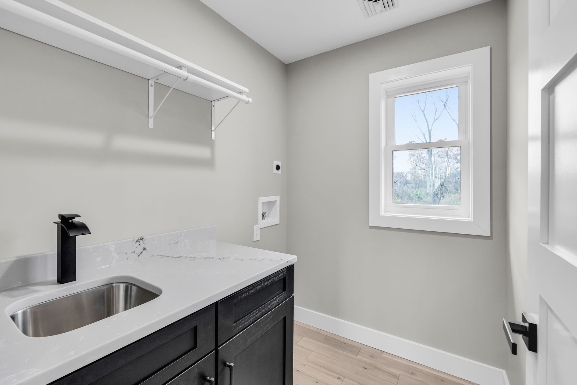 Laundry room with black cabinets, white countertop, stainless steel sink, window, and hanging rod.