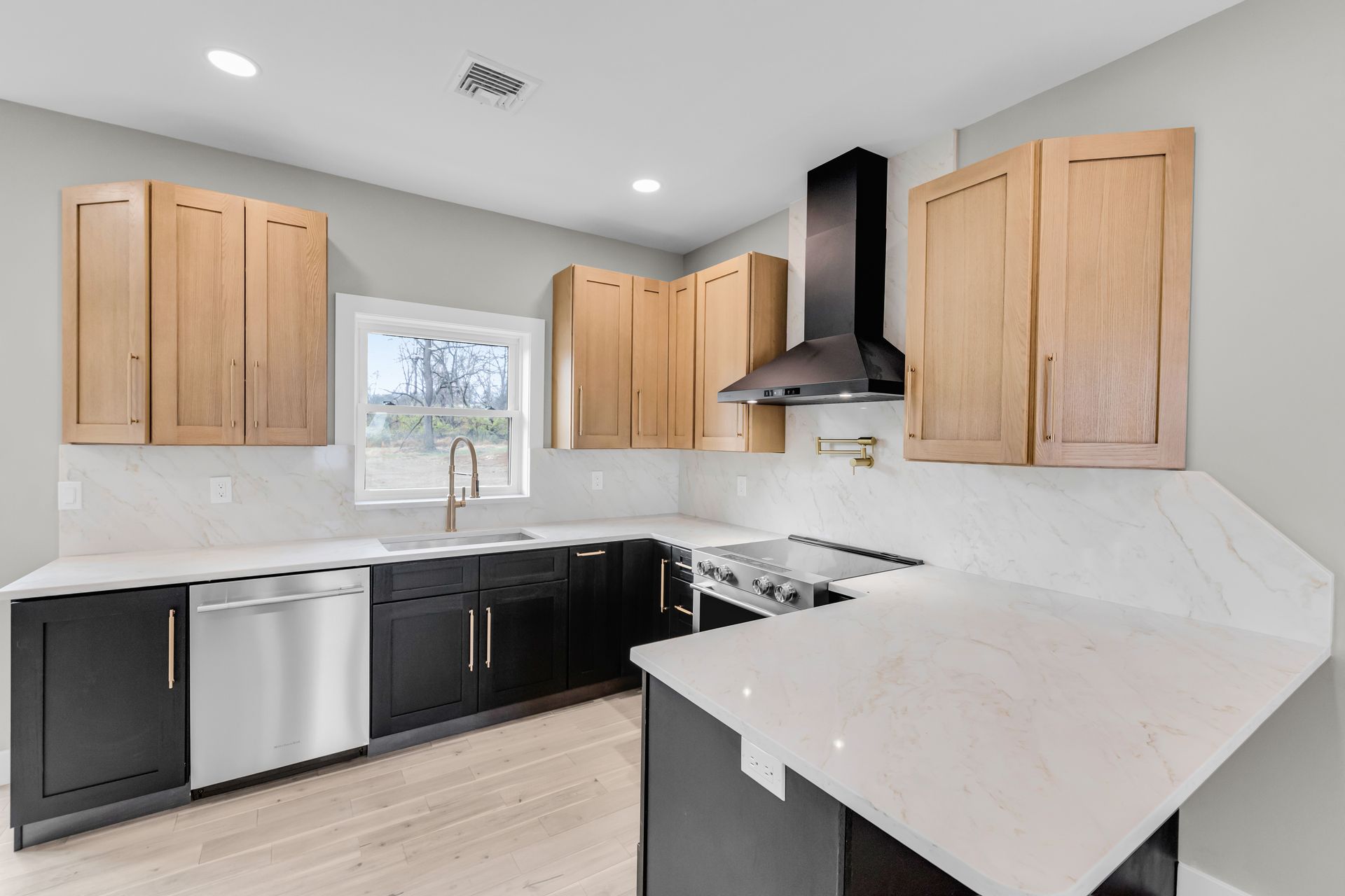 Modern kitchen with light wood upper cabinets, dark lower cabinets, and white countertops.