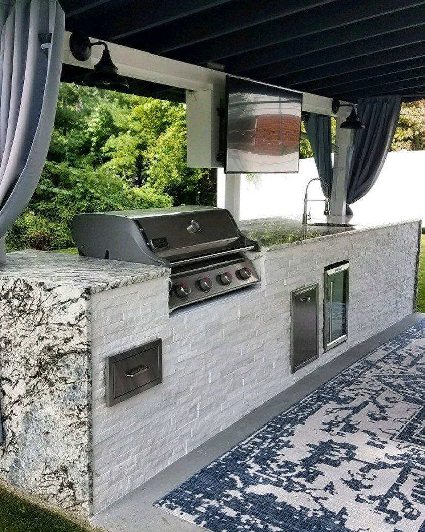 An outdoor kitchen with a grill , sink , and television.