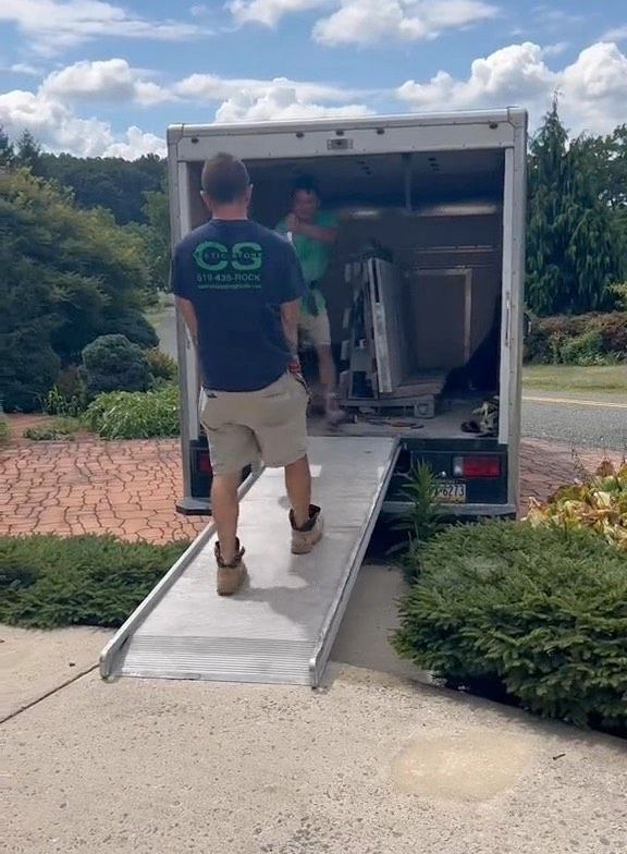 A man in a cs shirt is walking down a ramp towards a moving truck.