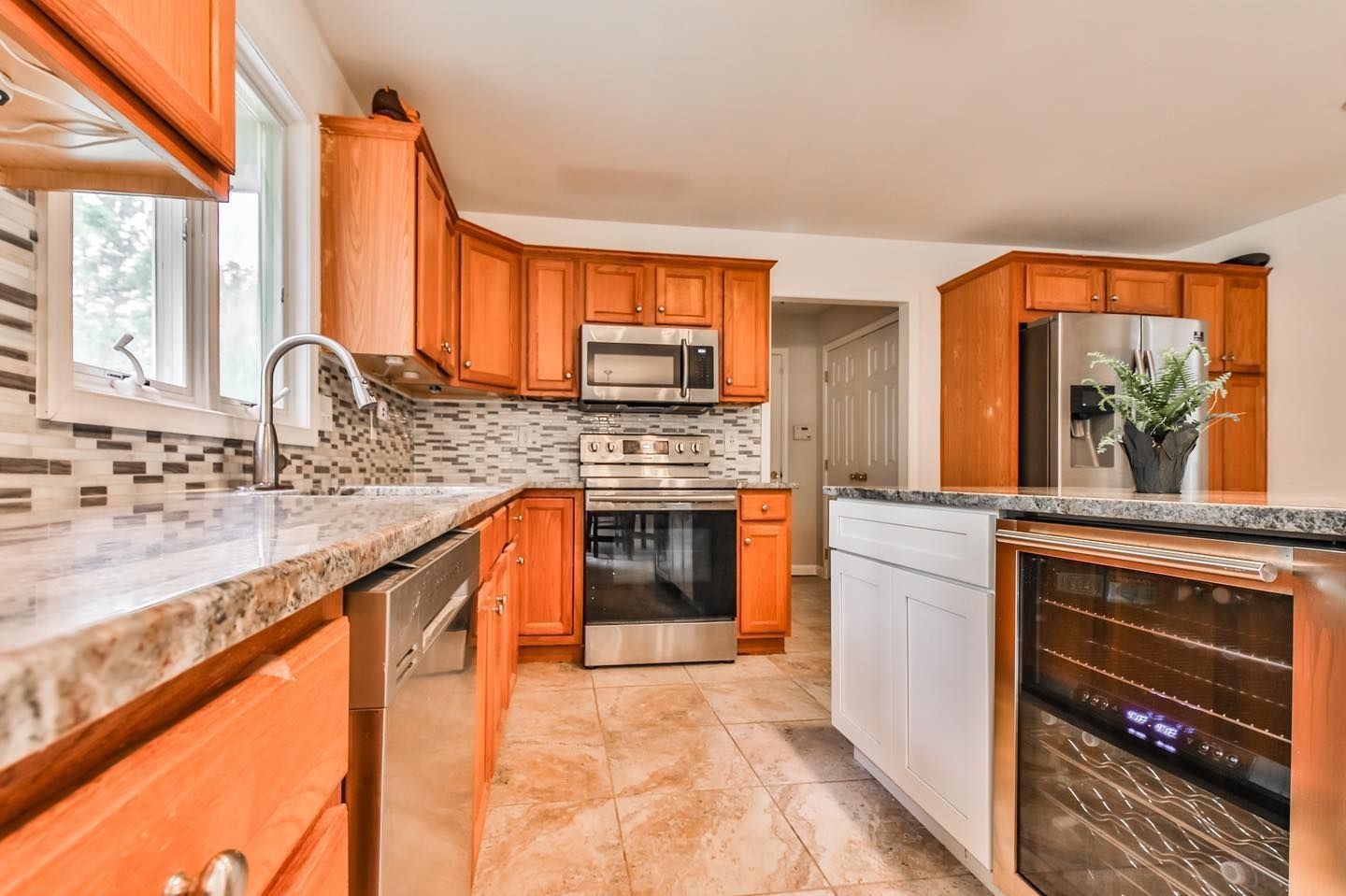 A kitchen with wooden cabinets , stainless steel appliances , granite counter tops and a wine cooler.