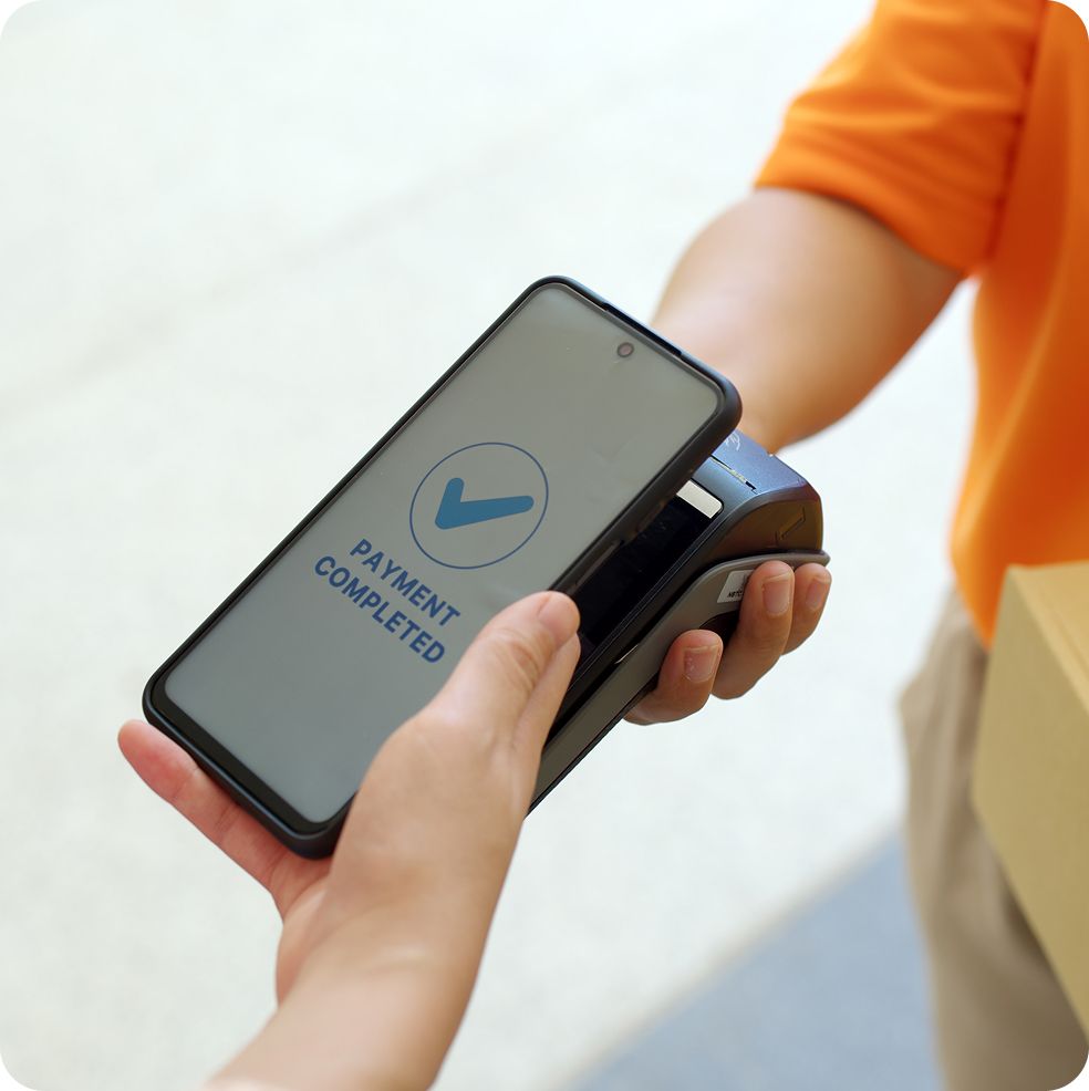 Person paying with phone; payment completed on device. Orange shirt, light background.