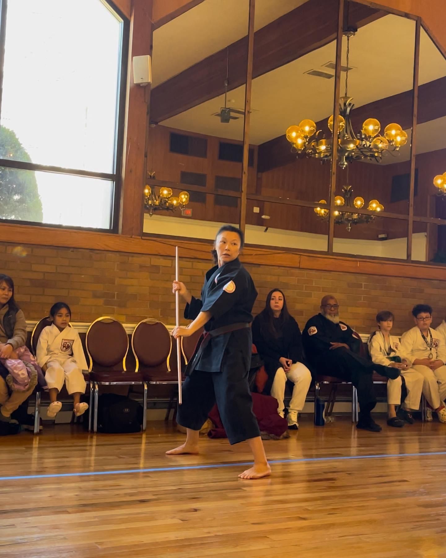 A man is holding a stick in a room with people sitting in chairs.