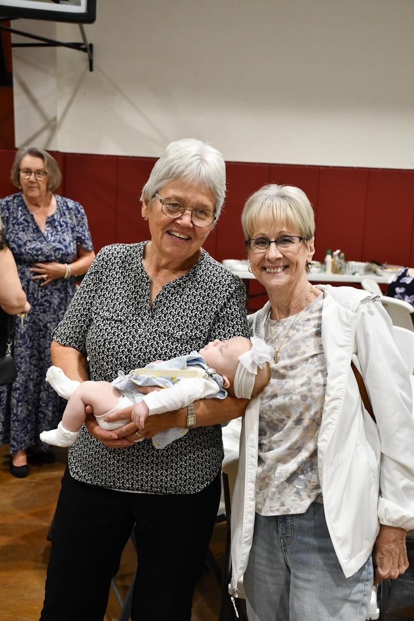 Two women are standing next to each other holding a baby.