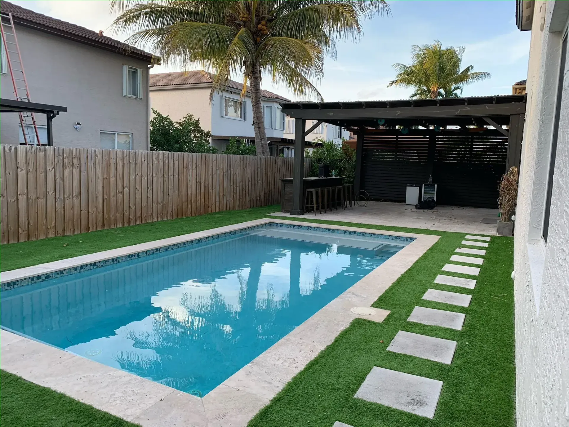 Modern backyard swimming pool with artificial turf designed by swimming pool construction company in South Florida
