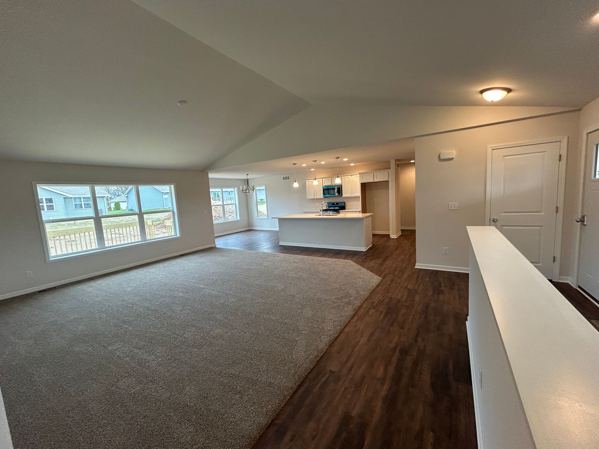 Interior view of a house with a living area, kitchen, and entryway. Neutral colors and a large window.