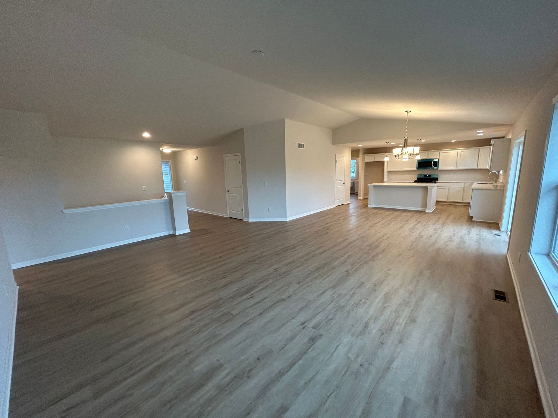 Empty modern open-plan living room with wood floors, white walls, and a kitchen in the background