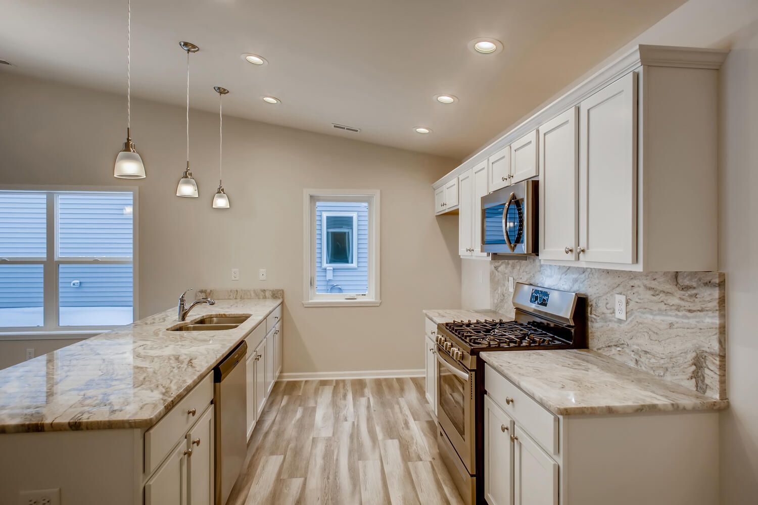 Modern kitchen with white cabinets, granite countertops, and stainless steel appliances; a window lets in daylight.