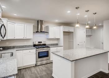 White kitchen with stainless steel appliances, granite countertops, and island with pendant lights.