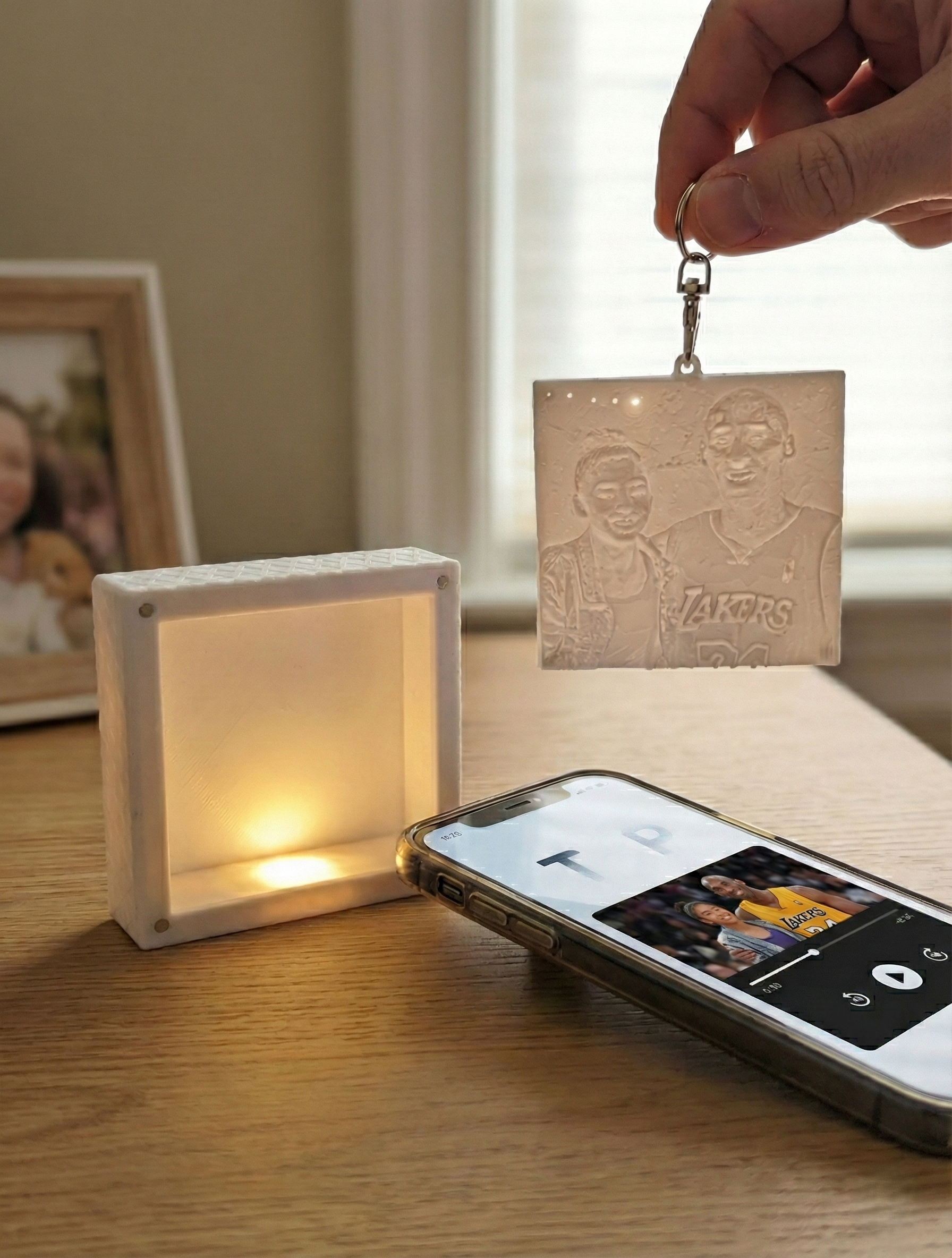 Keychain with etched image of Kobe Bryant and daughter, held in hand near a brown purse outdoors.