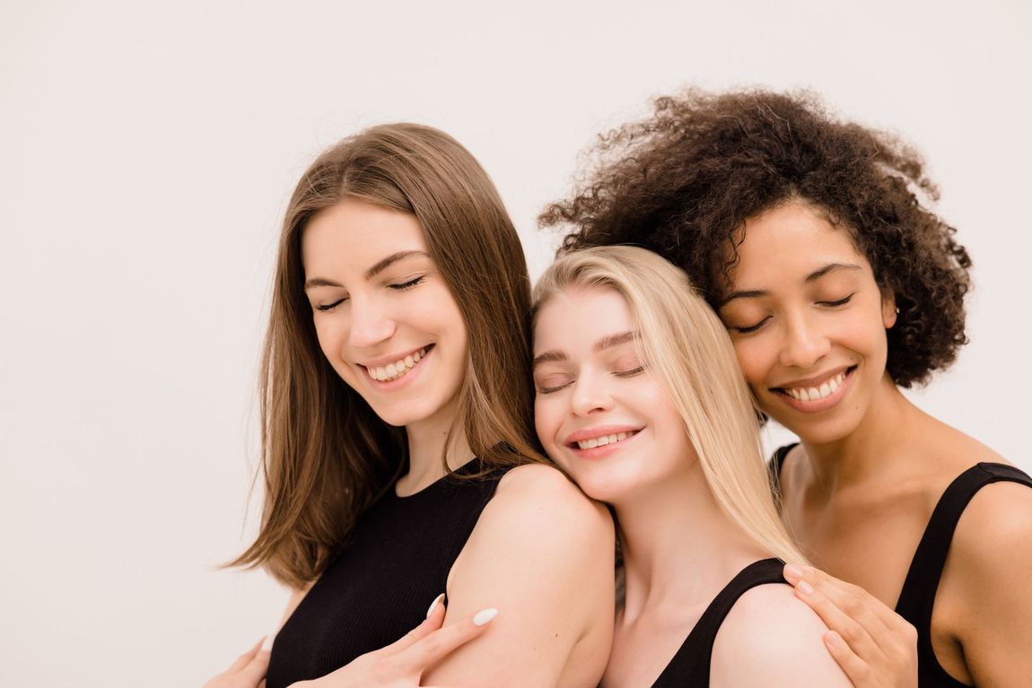 Three smiling friends posing closely together against a light background