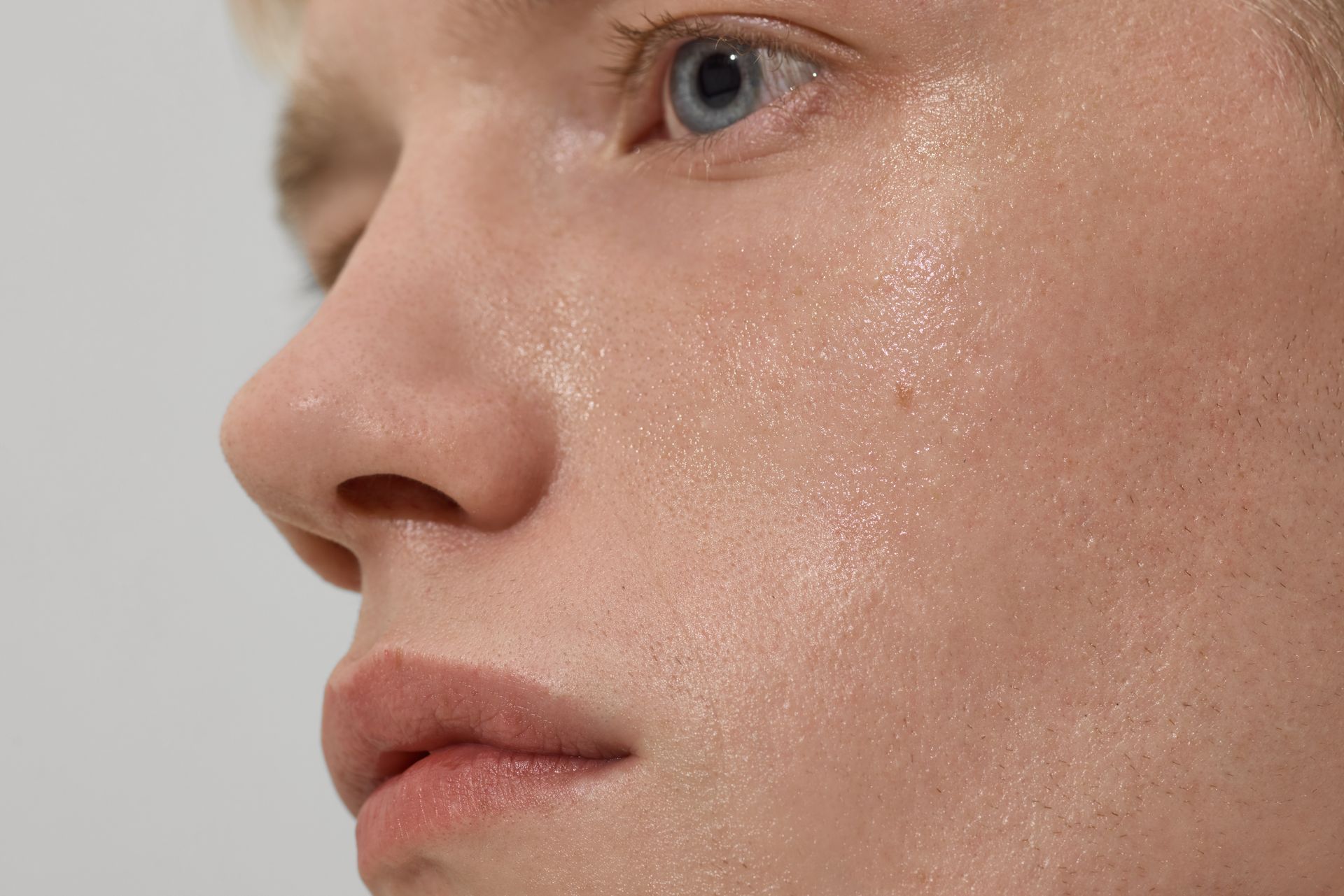 Close-up profile of a person’s face with dewy skin and blue eye against a light background
