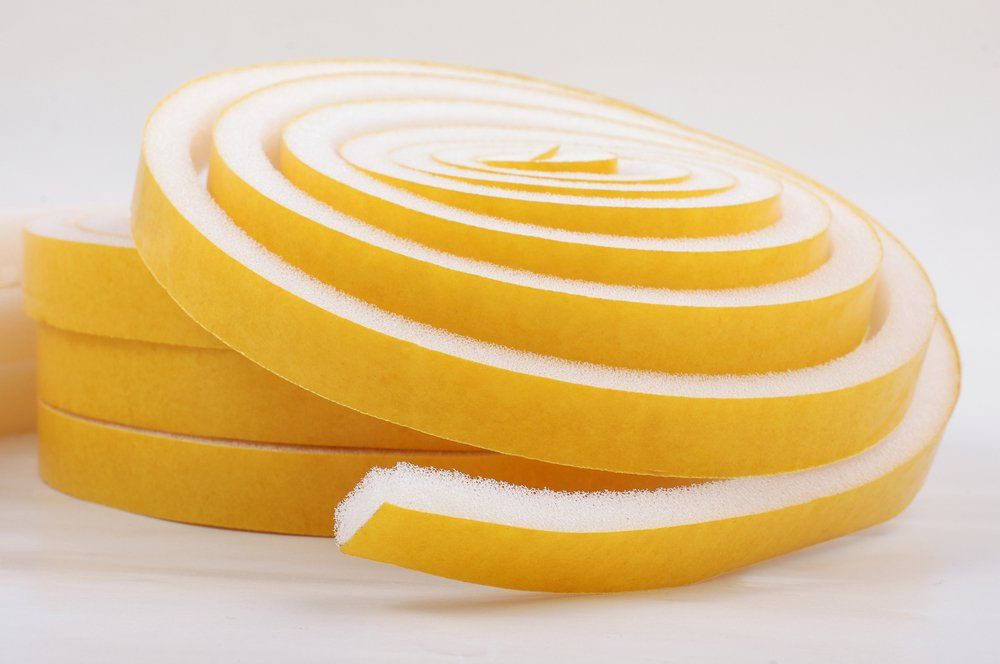 Eine Spule mit gelbem und weißem Schaumstoffklebeband auf einer weißen Oberfläche.