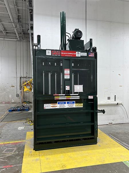 Green industrial trash compactor in a warehouse setting.
