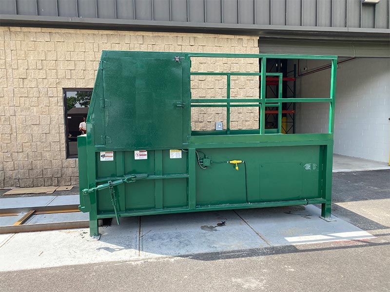 Green commercial trash compactor next to a beige brick building.