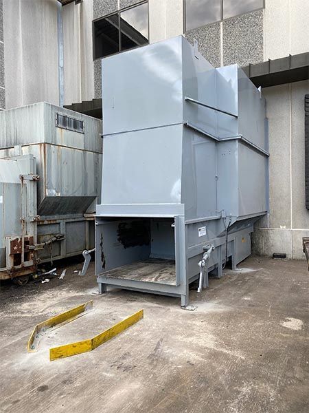 Large gray industrial air filtration system outdoors, near a building and metal containers.