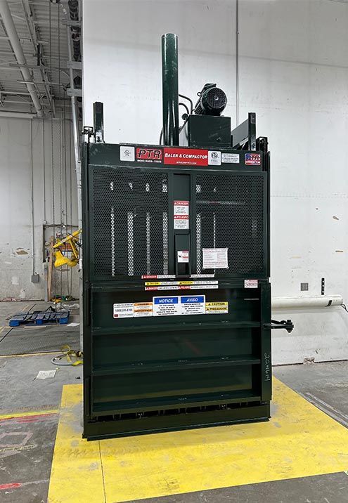 Green industrial cardboard baler in a warehouse.