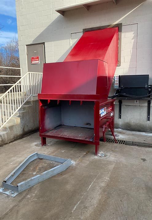 Green industrial cardboard baler in a warehouse.
