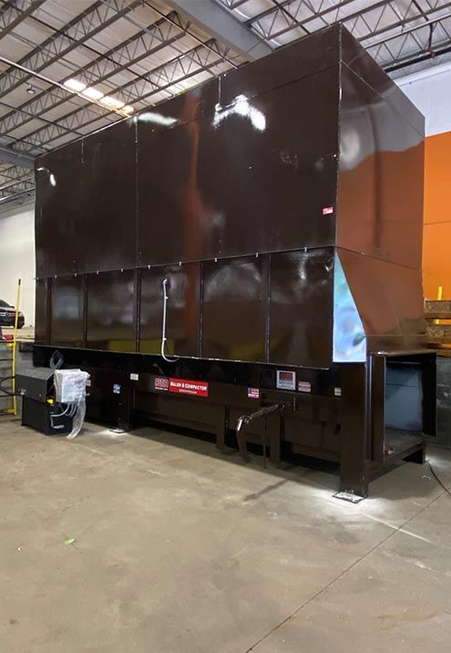 Large, dark brown industrial waste compactor inside a warehouse.