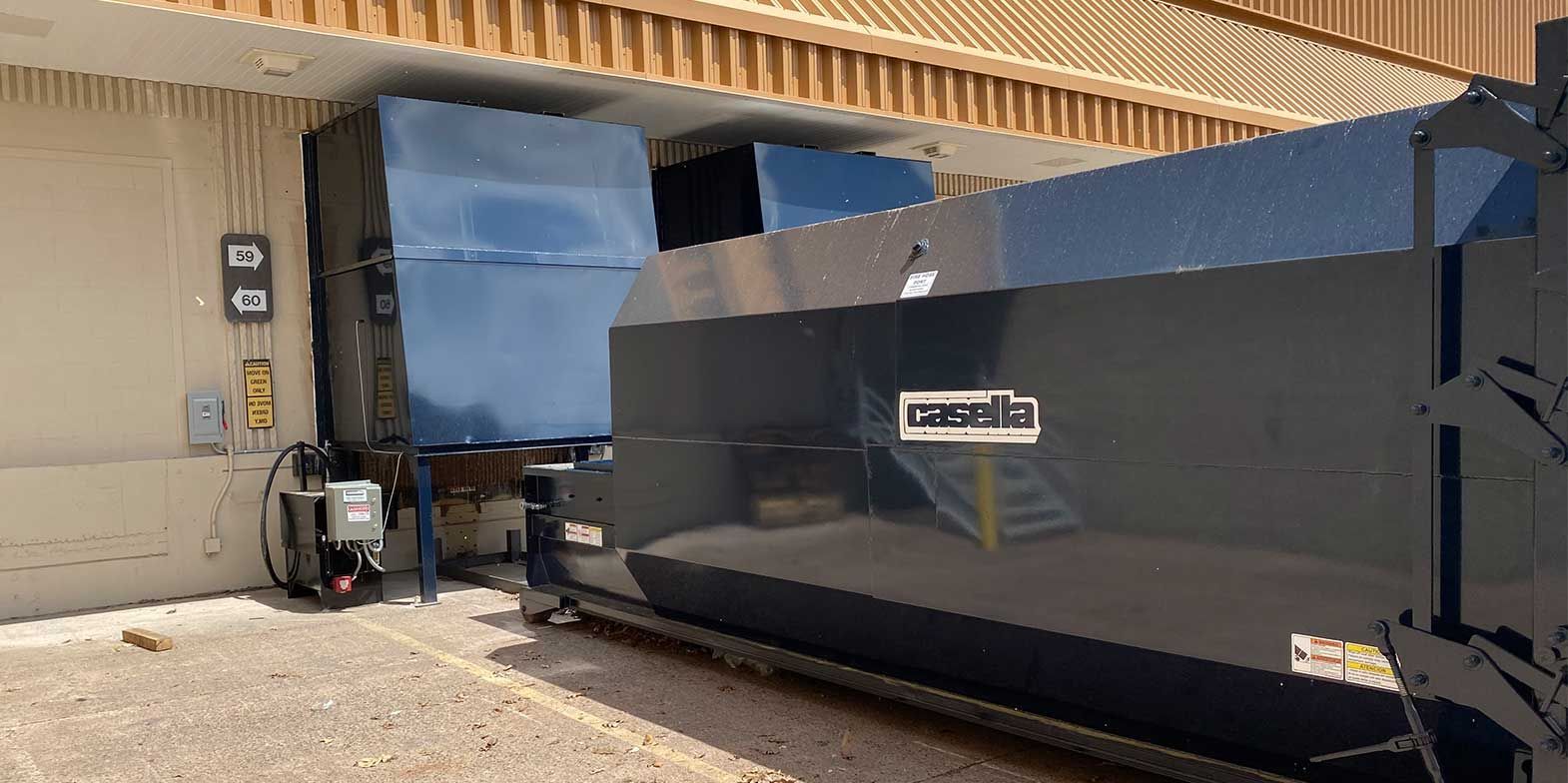 A large, dark dumpster and a compactor are next to a building.