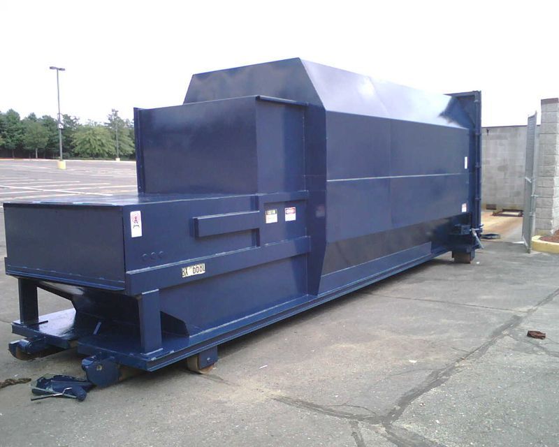Blue commercial trash compactor on wheels, outdoors in a parking lot.