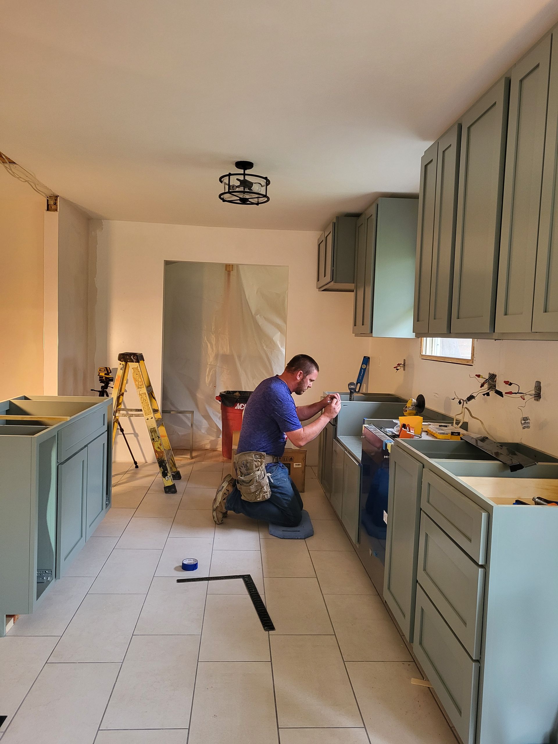 A man is kneeling in a kitchen working on a sink.