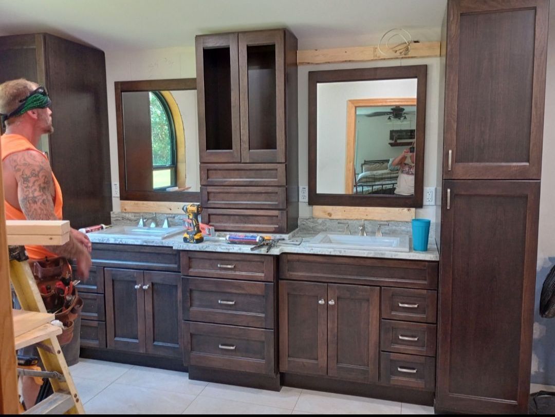 A man is standing on a ladder in front of a bathroom vanity.