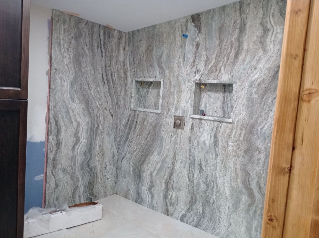 A bathroom with a marble wall and two shower niches.