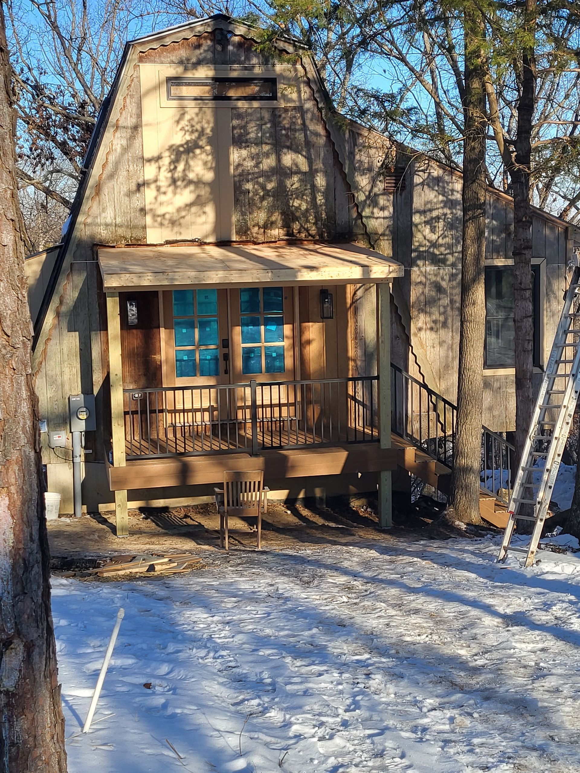 A small house with a porch and stairs in the snow.
