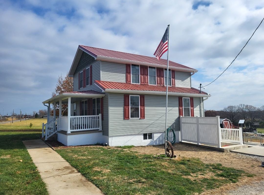 A large white house with red shutters and an american flag on top of it.