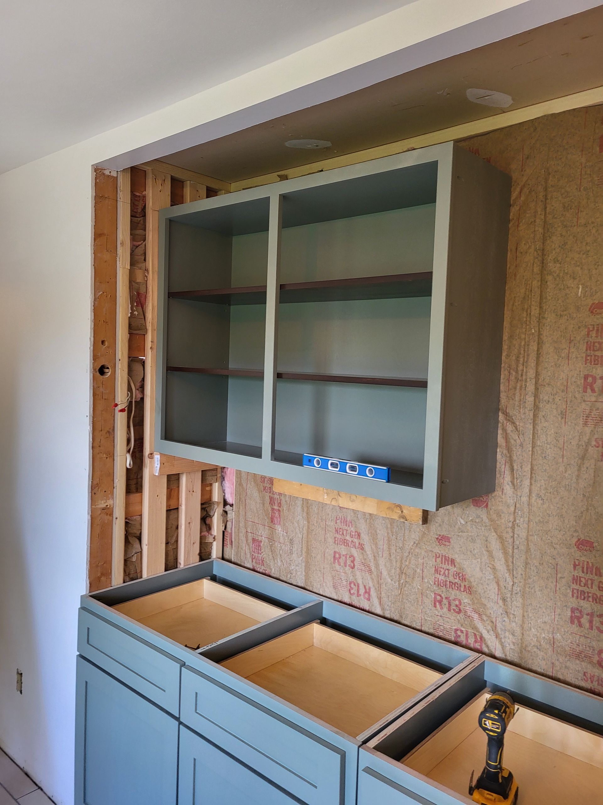 A kitchen under construction with blue cabinets and a drill