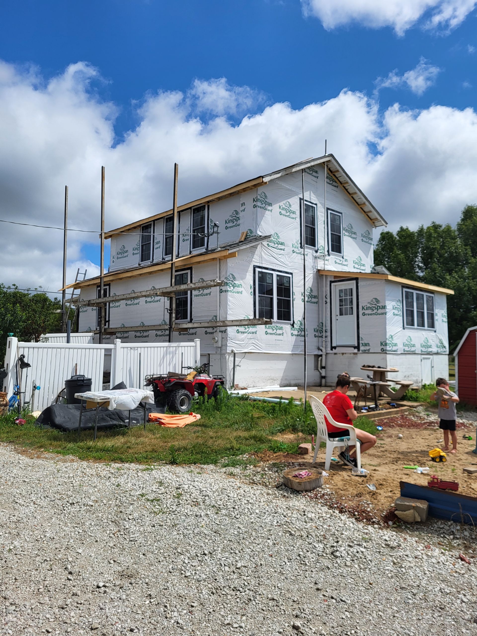 A man is sitting on a chair in front of a house under construction.