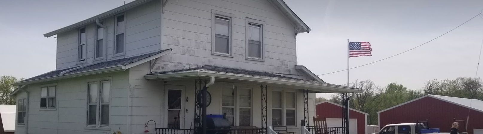 A white house with a red barn in the background and an american flag flying in front of it.