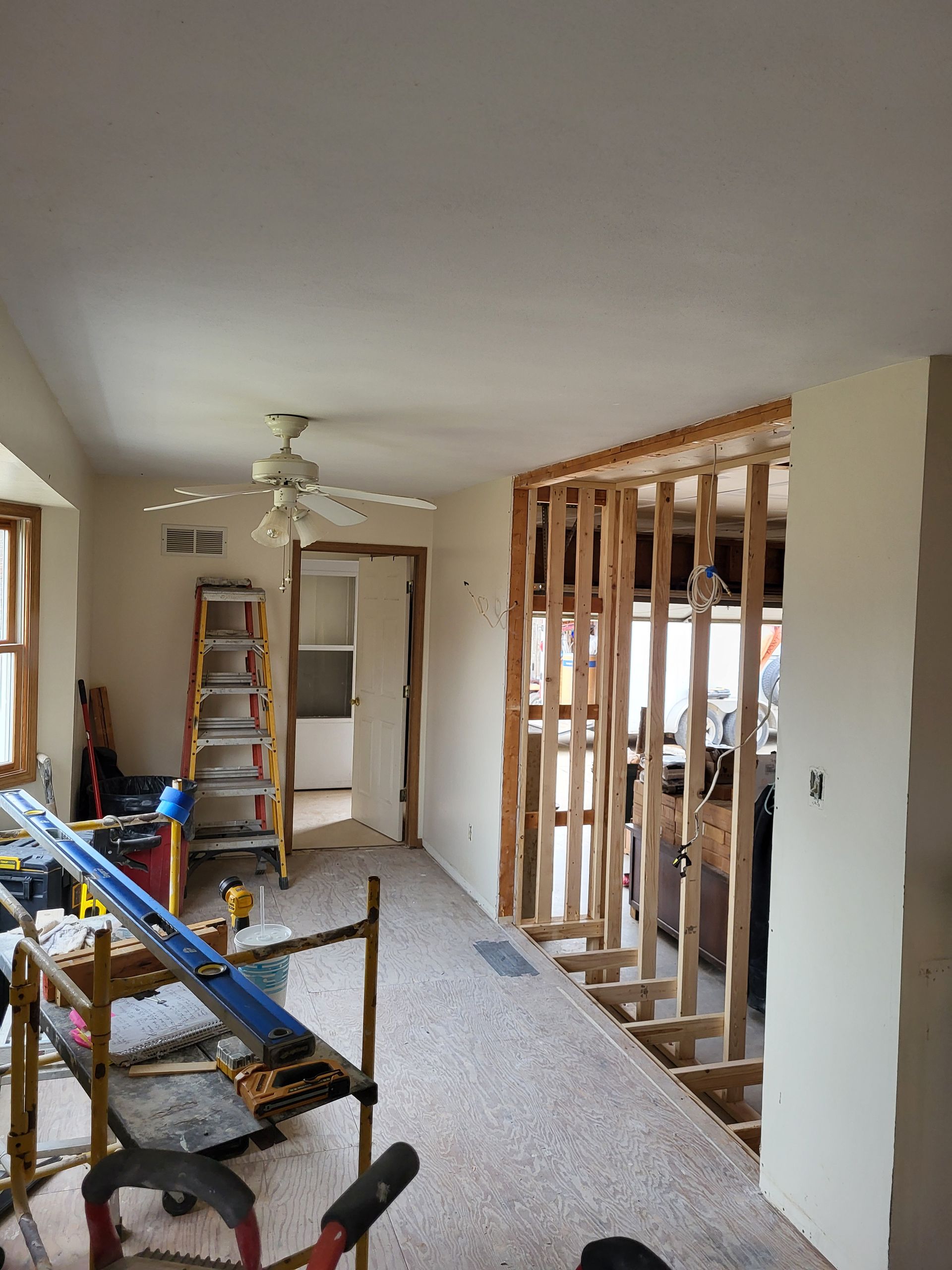 A living room under construction with a ceiling fan and a ladder.