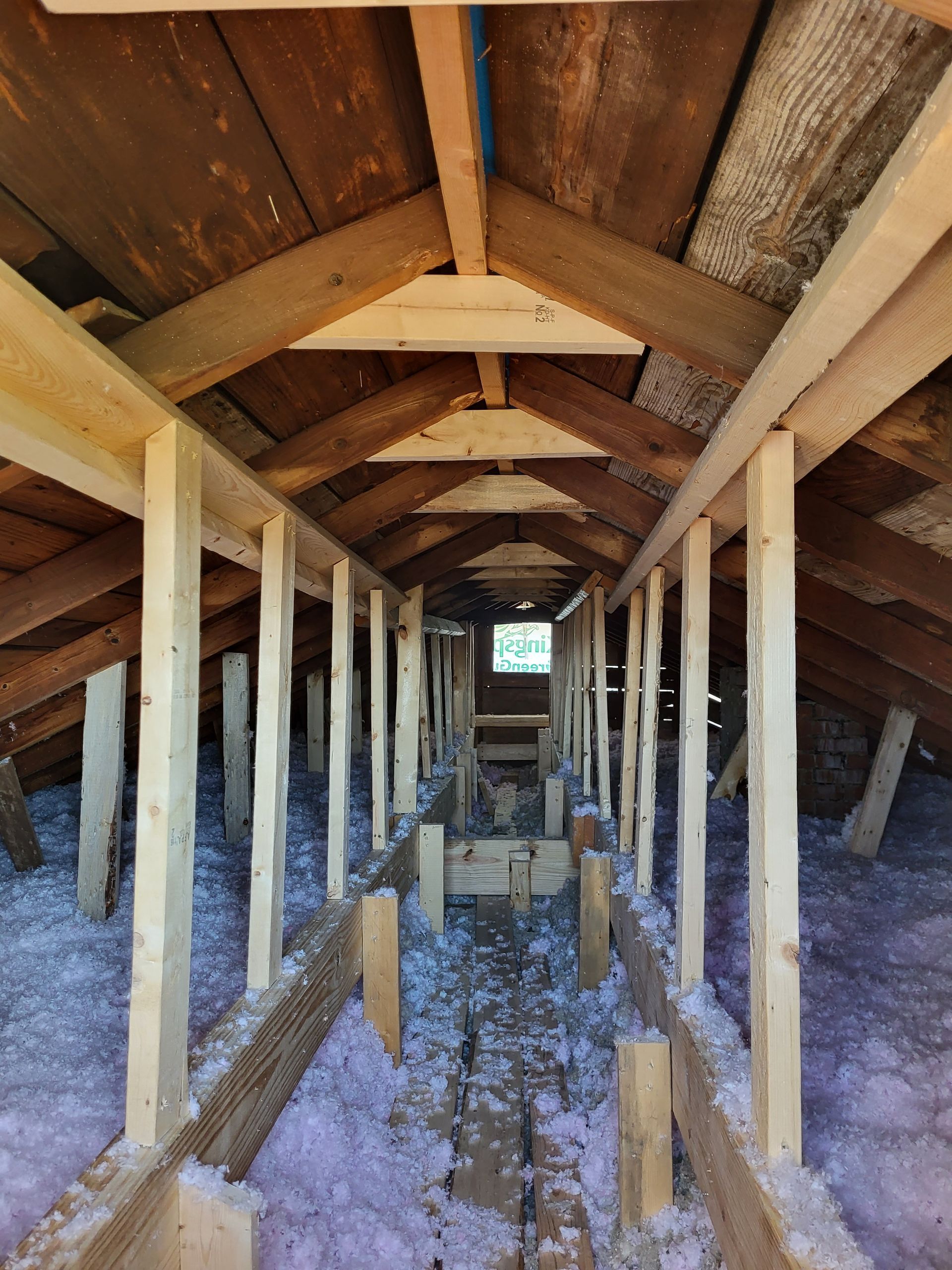 The attic of a house under construction with wooden beams and insulation.
