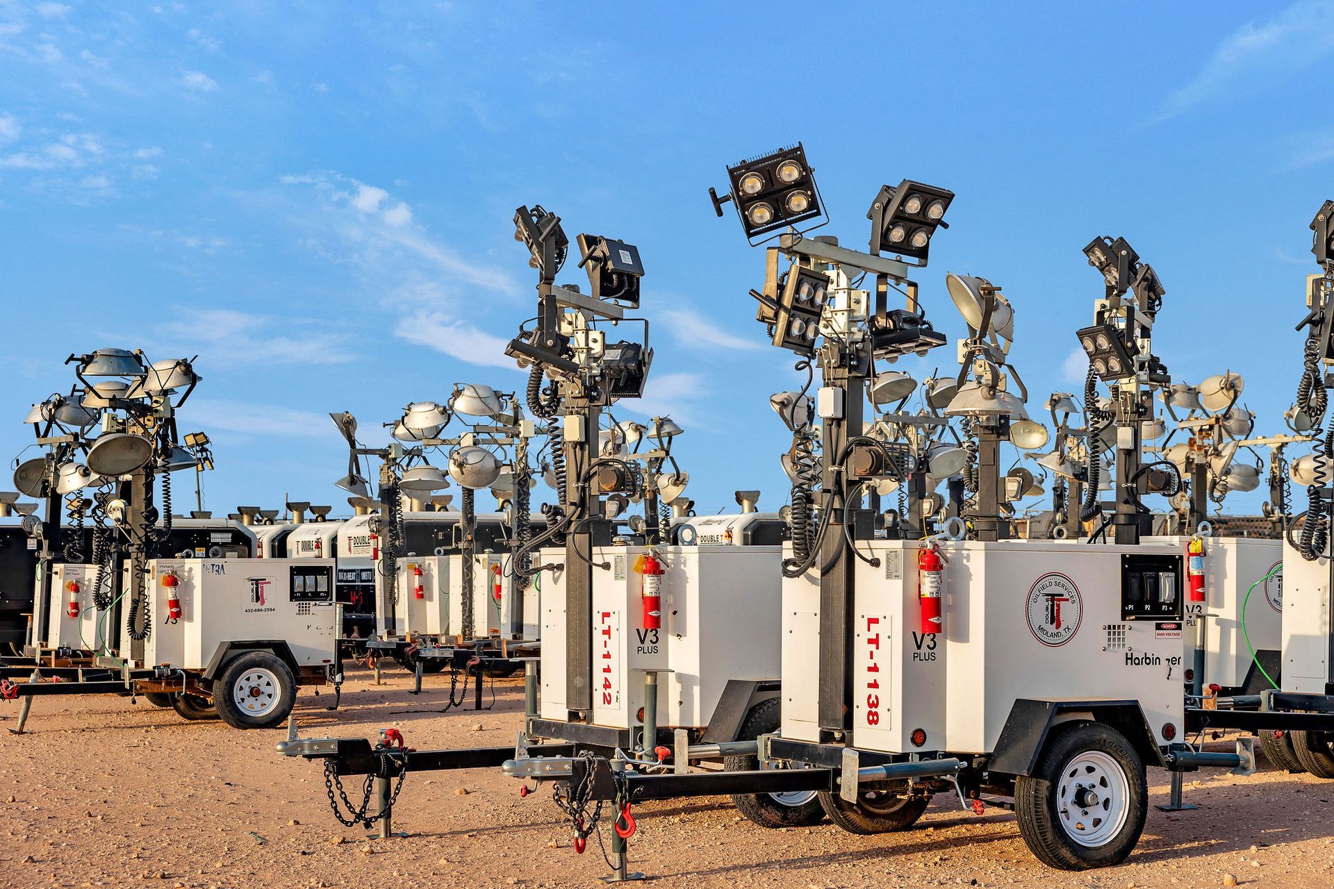 Several white light towers with multiple lights, parked outdoors.