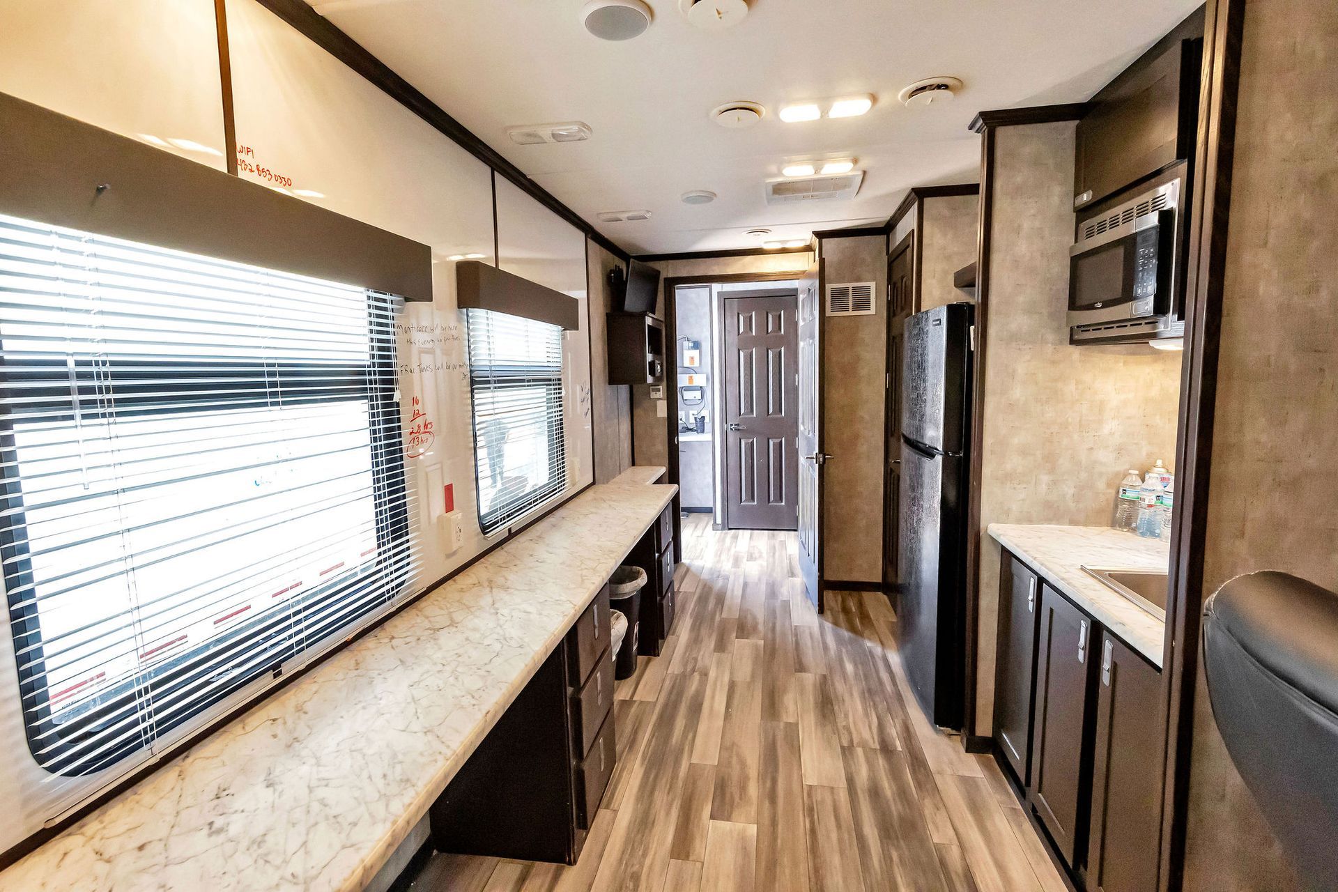 Interior view of a recreational vehicle with a long counter, windows, and kitchen appliances.