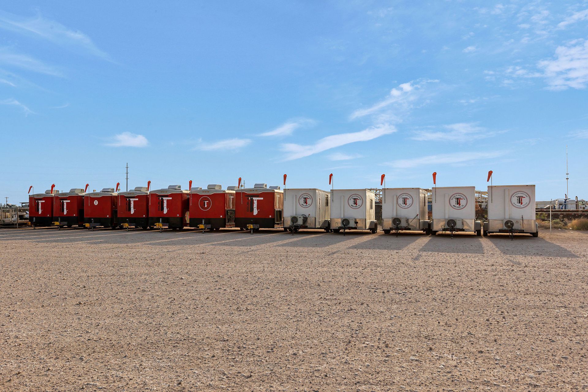 Red and white trailers parked on gravel under a blue sky.