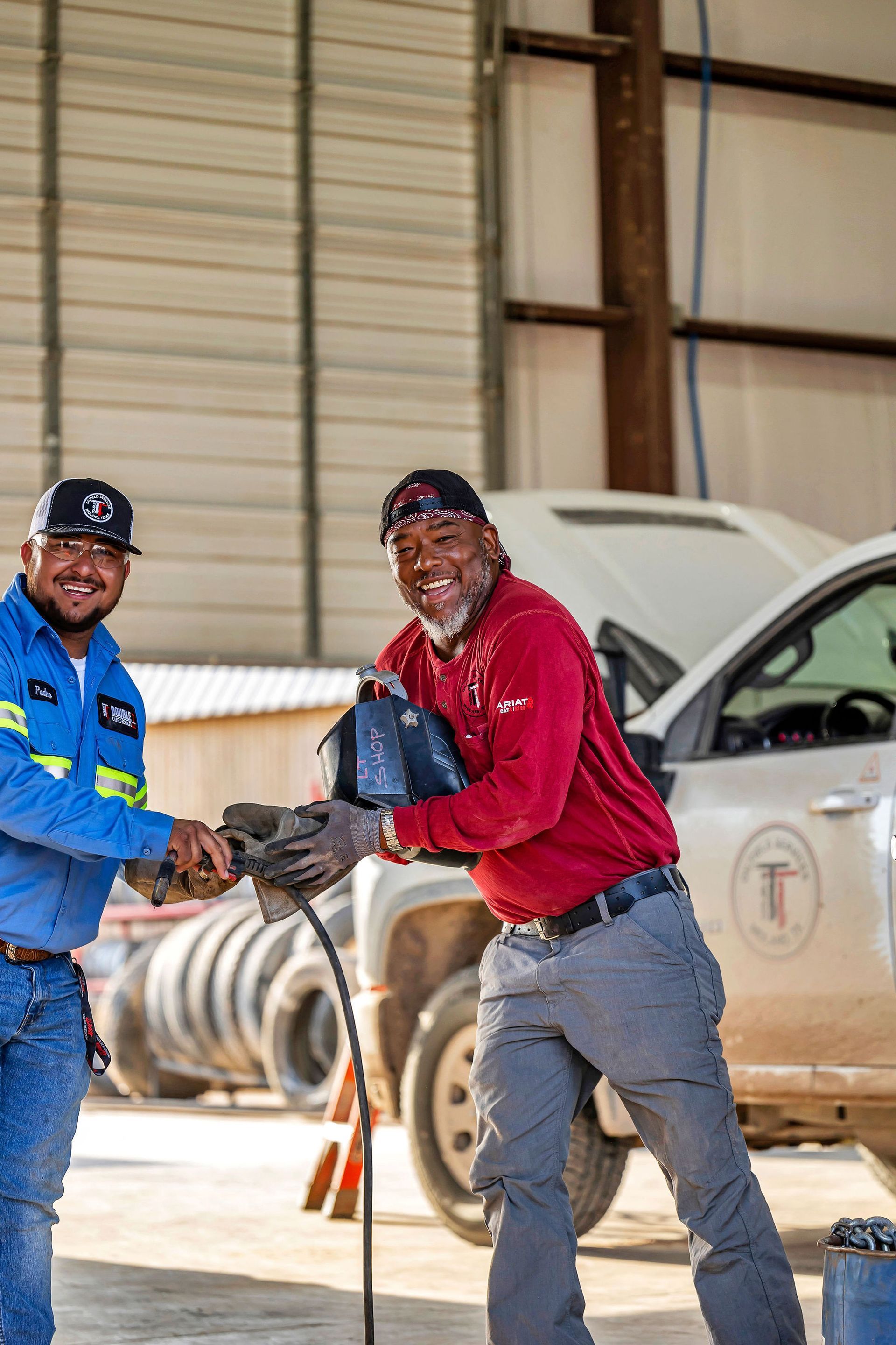 Two men shaking hands near a truck in a garage, one in red and the other in blue.
