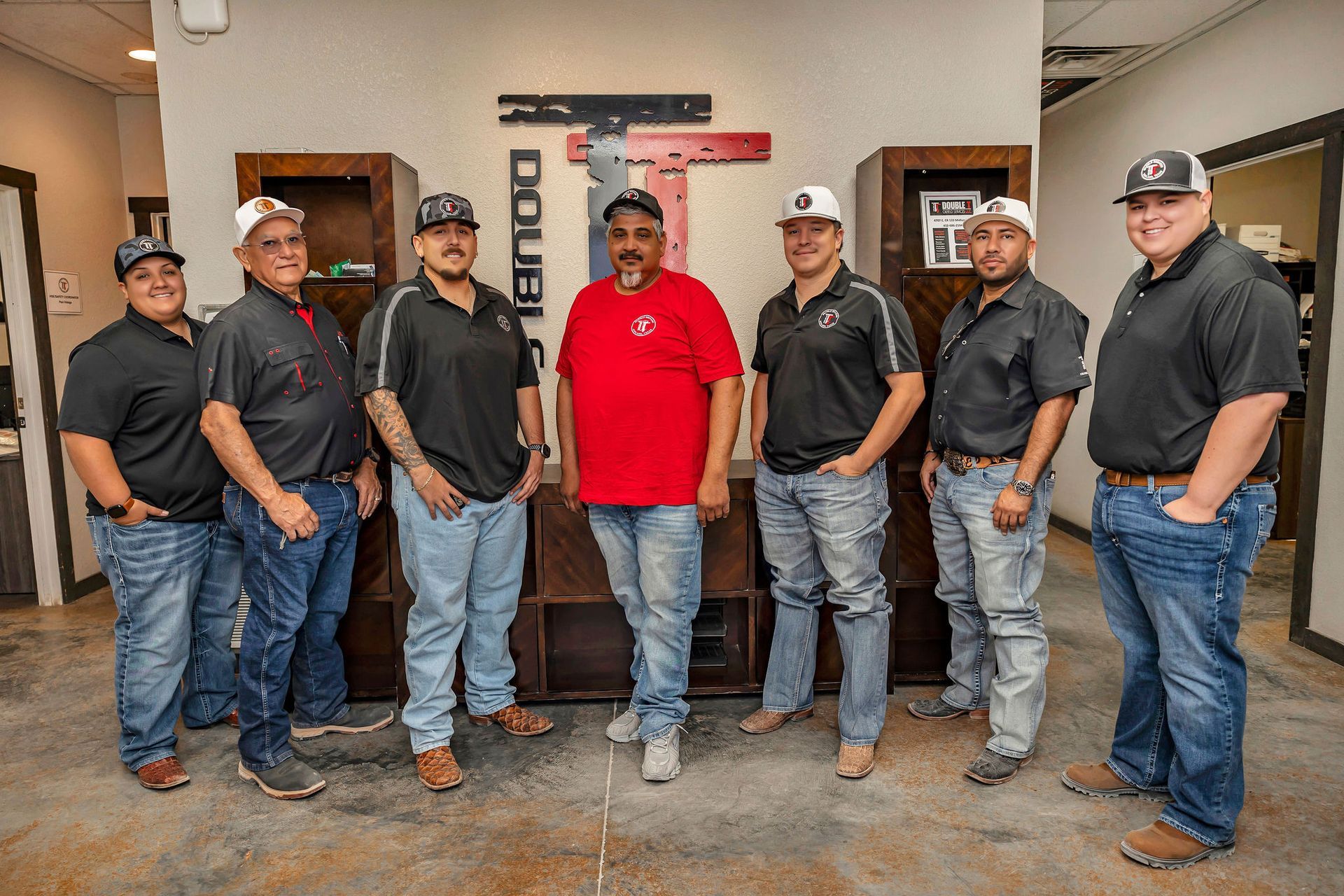 Group of eight men smiling inside, in front of a brown wall with 