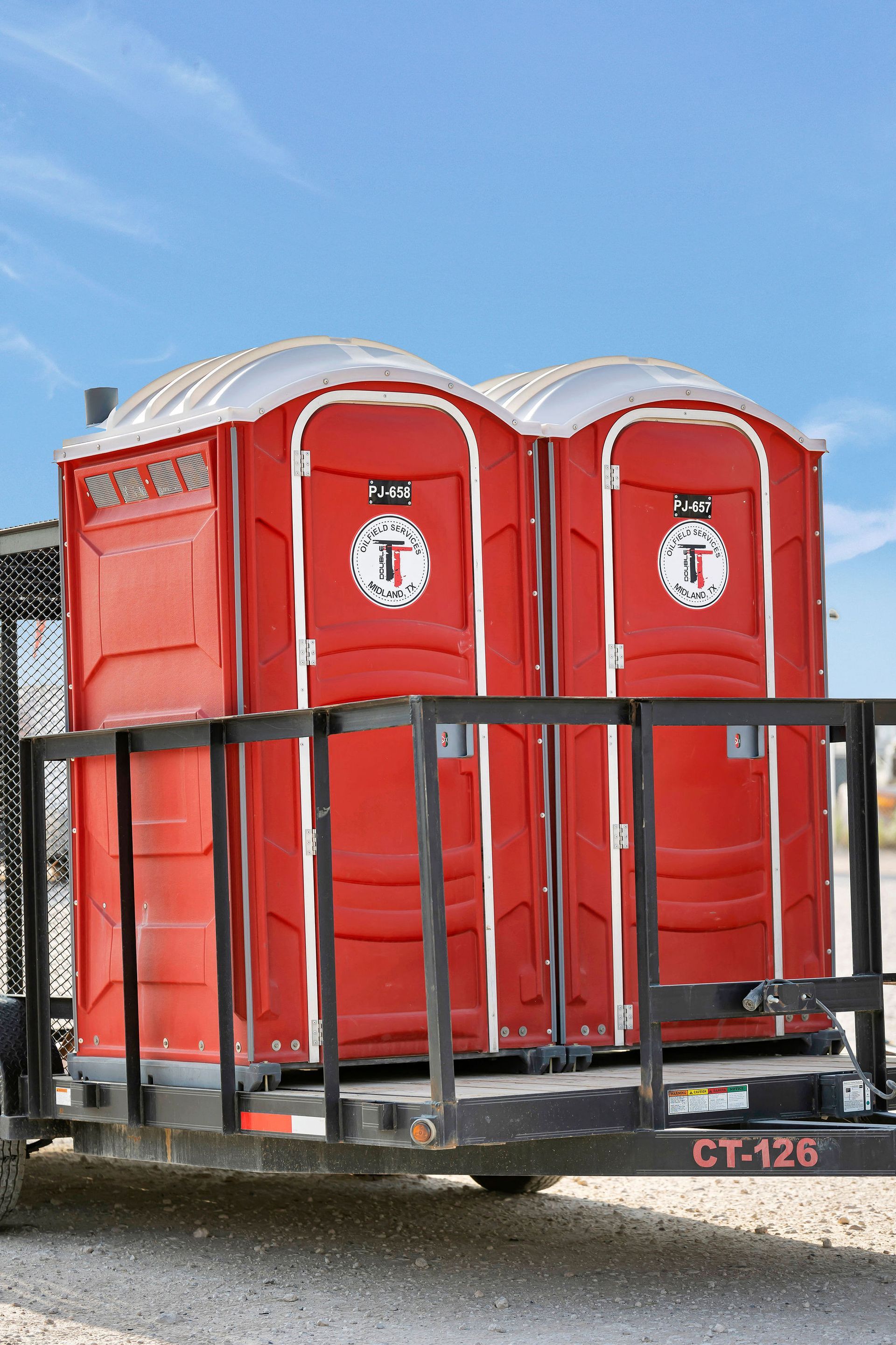 Two red portable toilets on a trailer, against a blue sky.