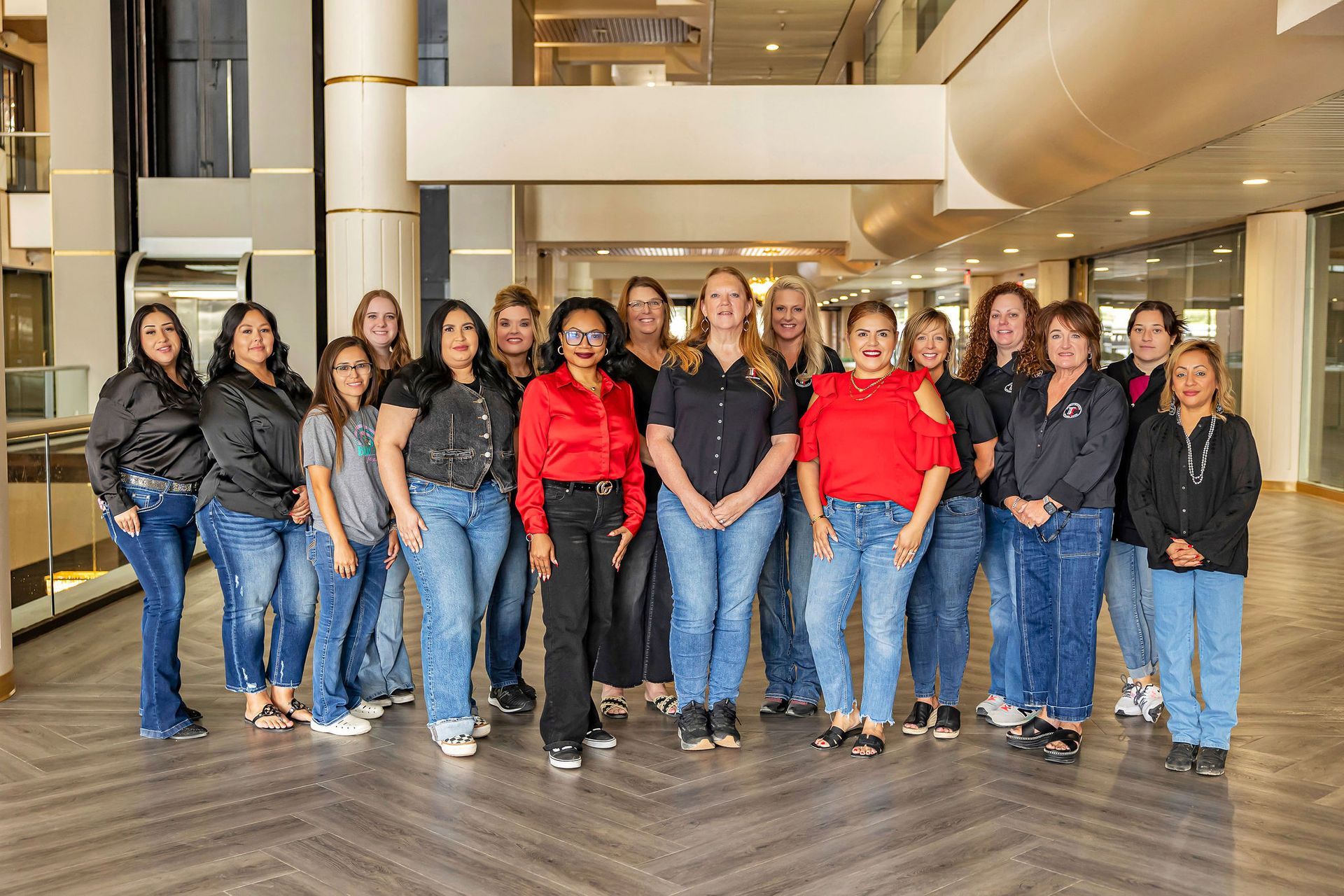 Group of diverse women smiling, posing indoors. Denim jeans, black and red shirts. Building interior.